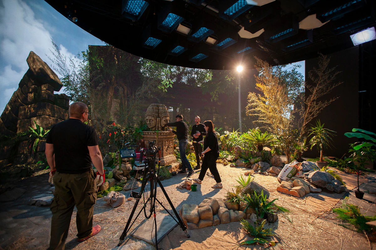 On set in front of the LED volume: a jungle temple on the screen, plants and rocks in the foreground set, and the crew by the camera