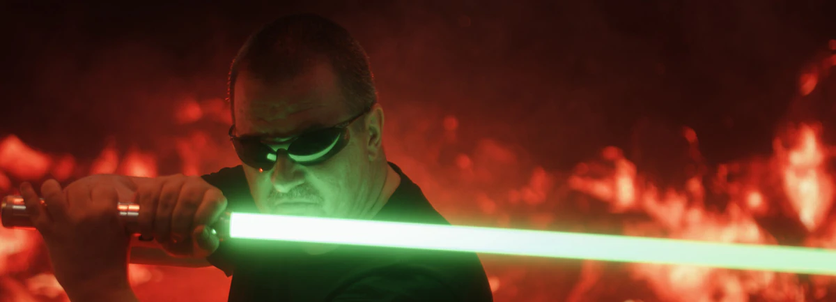 Shot: a man with a green lightsaber against fire