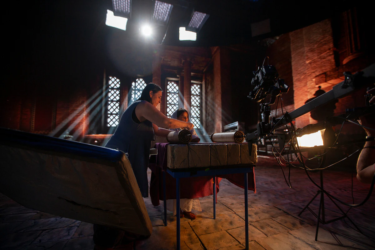 On set: a cathedral scene with lighting and a camera on a crane